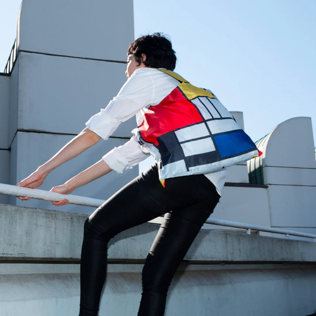 Torba LOQI Piet Mondrian na ramieniu osoby wspinającej się po barierce na tle budynków