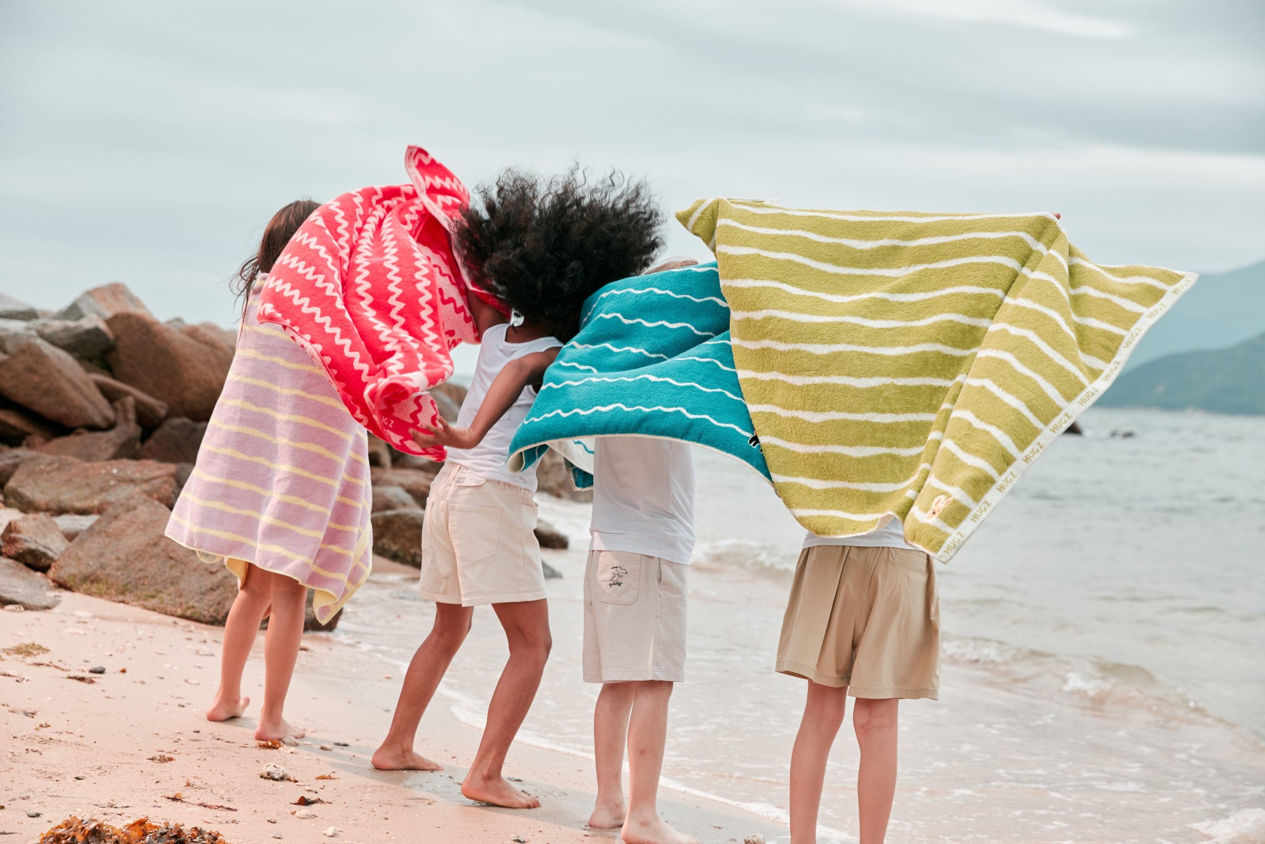 Cztery dzieci na plaży owinięte w kolorowe dwustronne ręczniki szybkoschnące firmy MOB