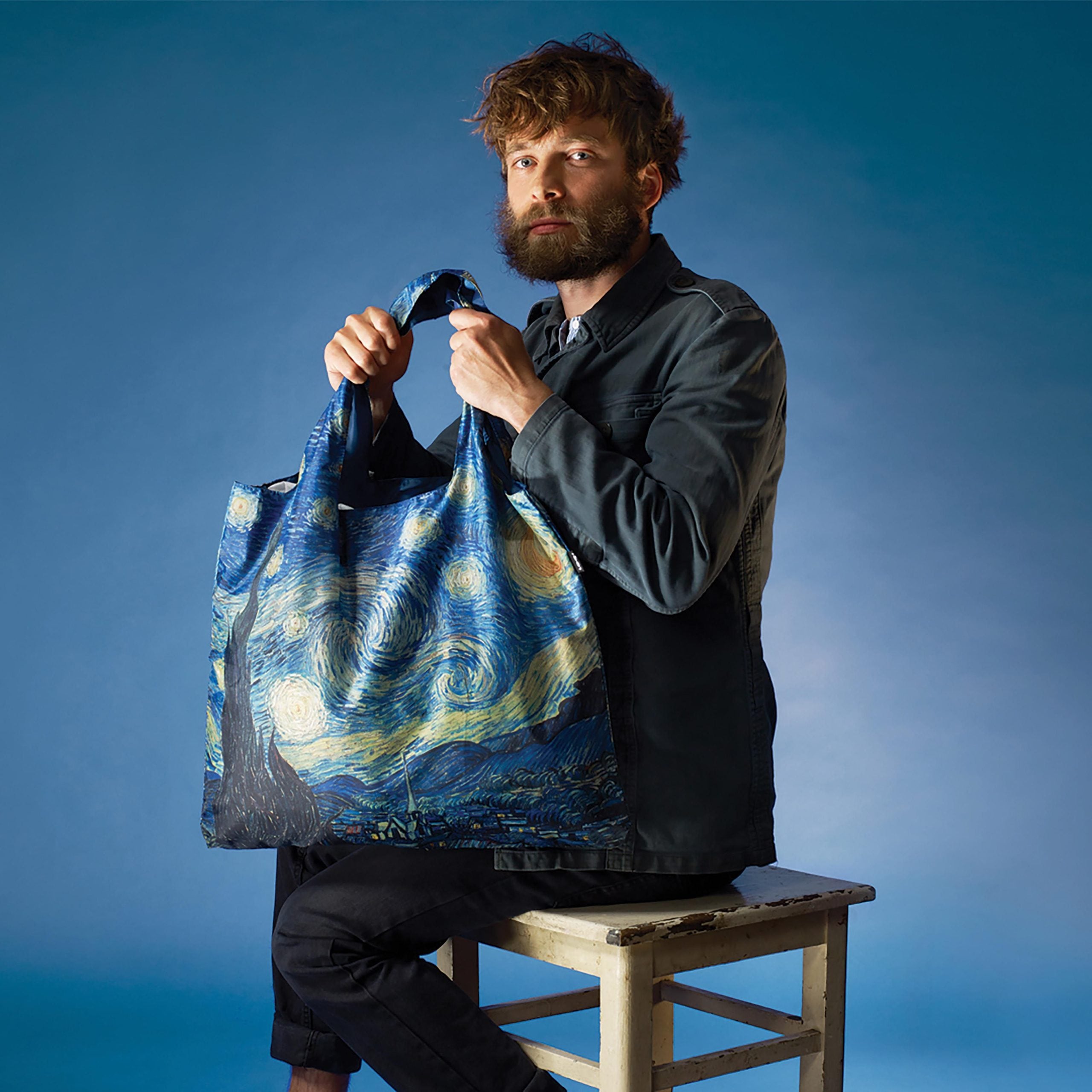 Torba podręczna Vincent van Gogh z nadrukiem Gwiaździstej nocy trzymana przez mężczyznę na niebieskim tle