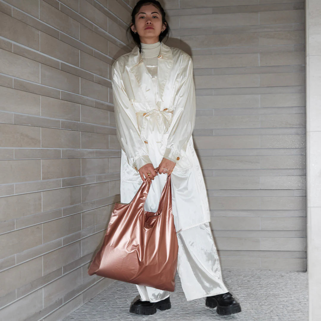 Kobieta trzymająca torba LOQI metallic rose gold w modnym białym płaszczu i czarnych butach