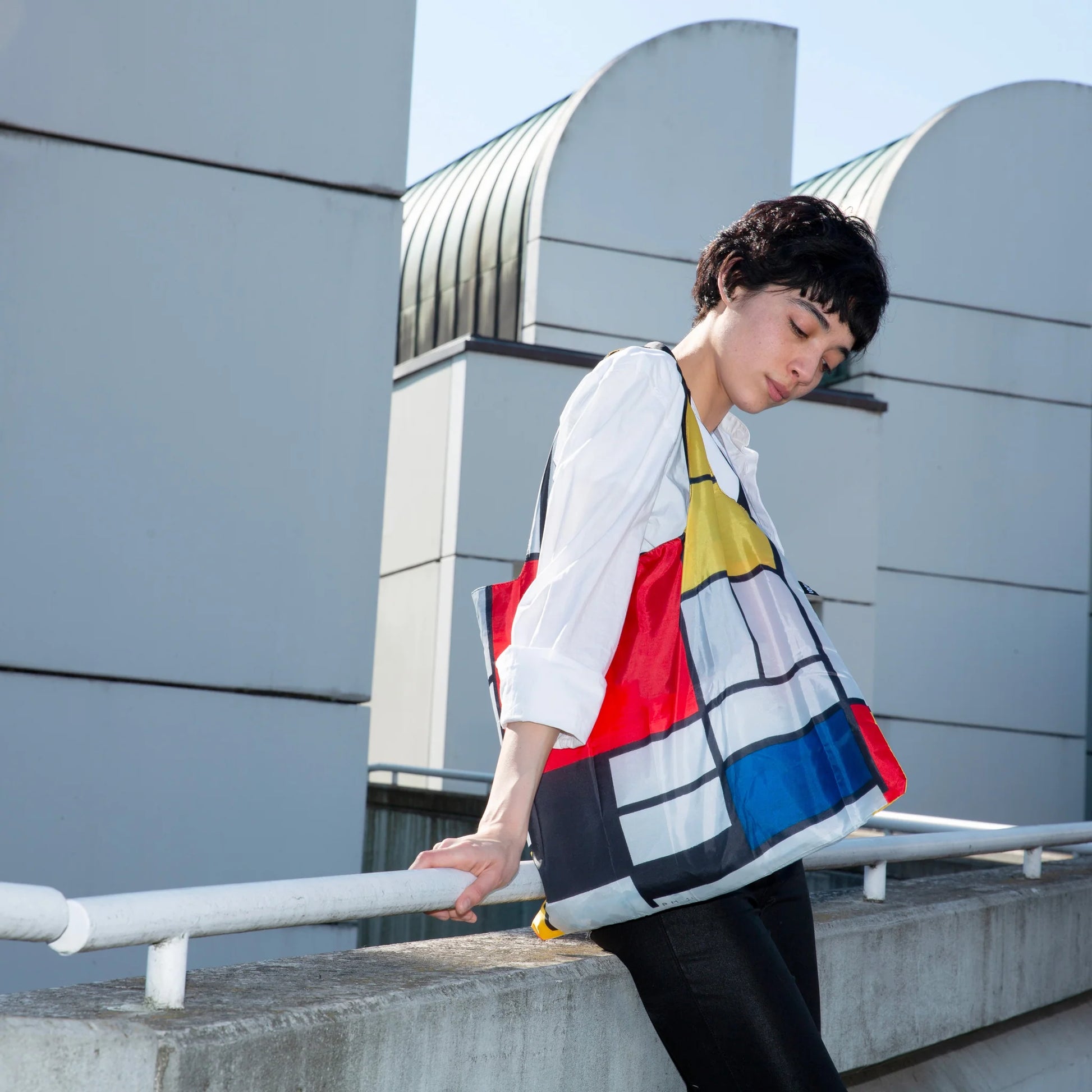 Kobieta z krótkimi włosami nosząca kolorową torbę LOQI Piet Mondrian na ramieniu na zewnątrz