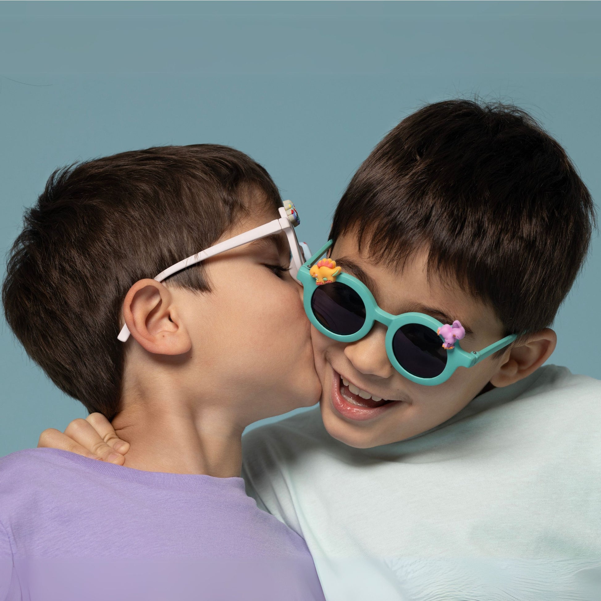 Dwóch chłopców bawiących się w okulary przeciwsłoneczne dla dzieci z ozdobami na turkusowych oprawkach