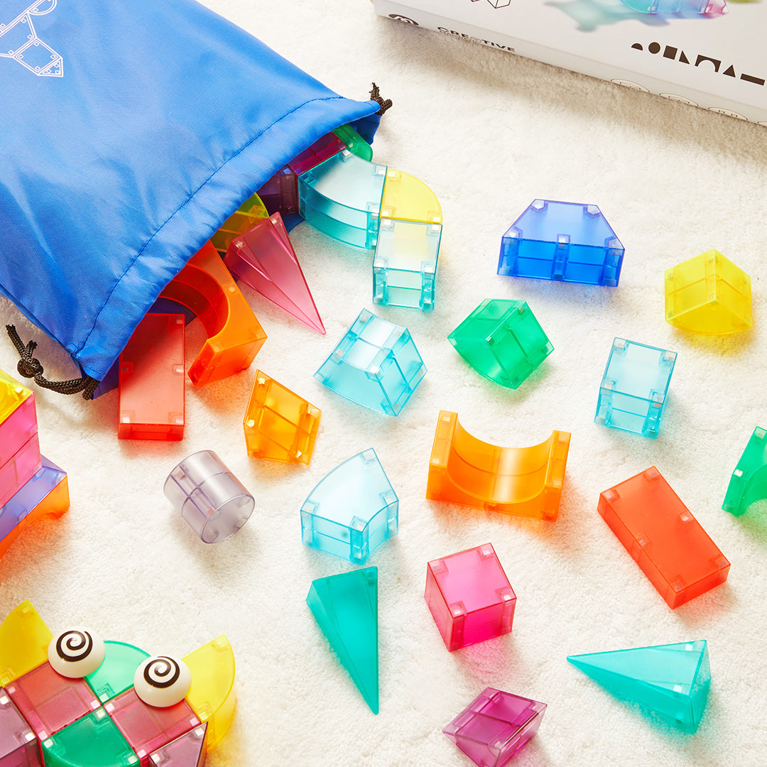 Kolorowe klocki magnetyczne 3D z przezroczystego plastiku rozsypane obok niebieskiego woreczka
