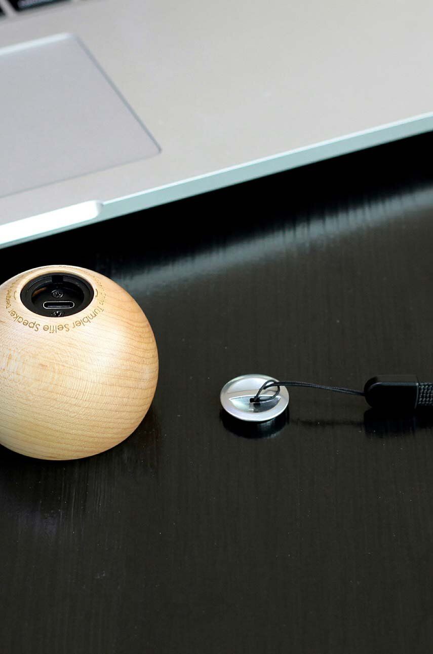 Głośnik bezprzewodowy drewniany w kształcie kuli obok laptopa na ciemnym blacie