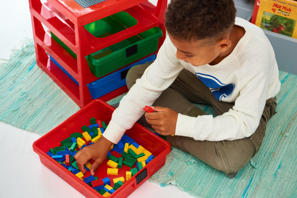 Chłopiec bawiący się klockami LEGO przy kolorowym regale LEGO z szufladami do przechowywania