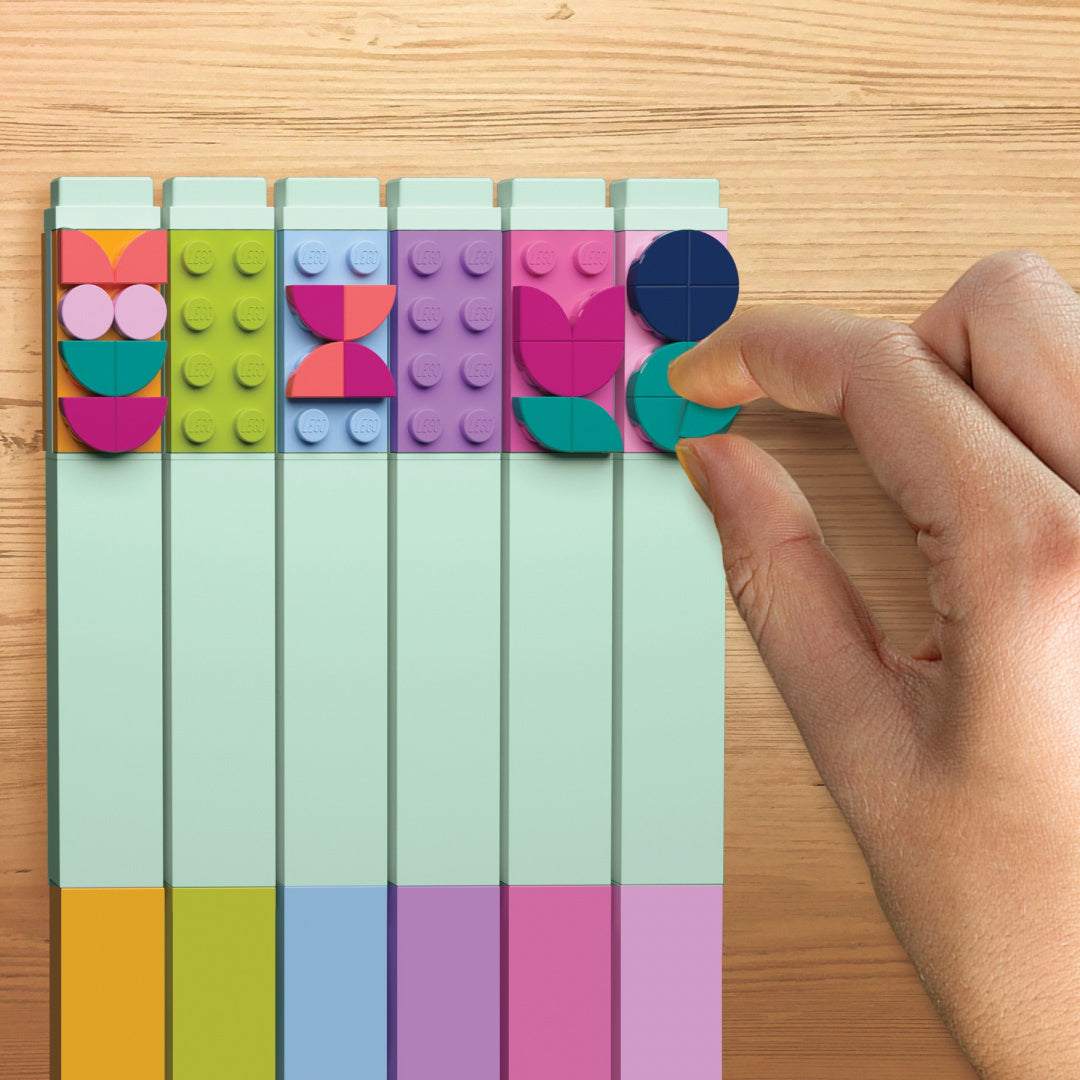 Ręka umieszczająca klocki na flamastrach LEGO DOTS z kolorowymi dekoracjami na drewnianym stole