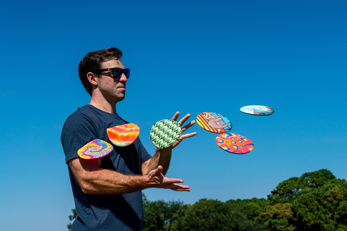Mężczyzna rzucający kolorowe frisbee Waboba Wingman na tle błękitnego nieba w parku