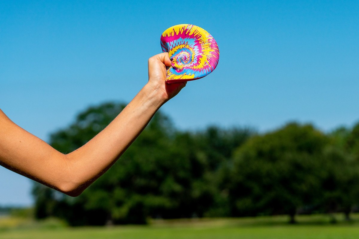 Kolorowy frisbee Waboba Wingman chwytany ręką na tle zielonego parku i niebieskiego nieba
