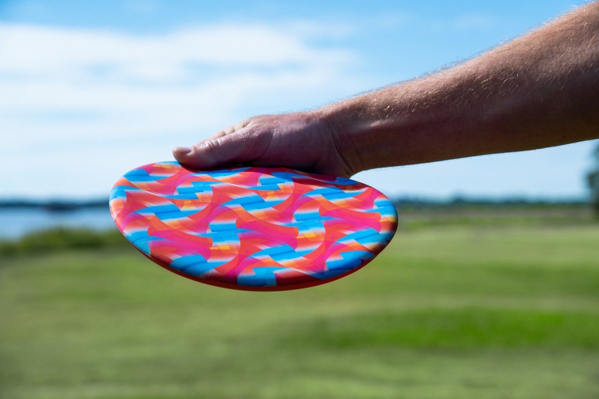 Kolorowy frisbee Waboba Wingman Pro trzymany przez dłoń na tle zielonej trawy i nieba