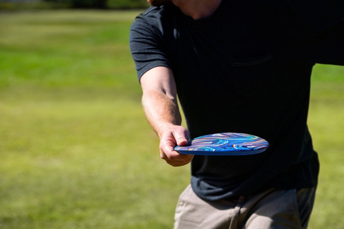 Mężczyzna rzucający frisbee Waboba Wingman Pro na zielonym trawniku podczas słonecznego dnia