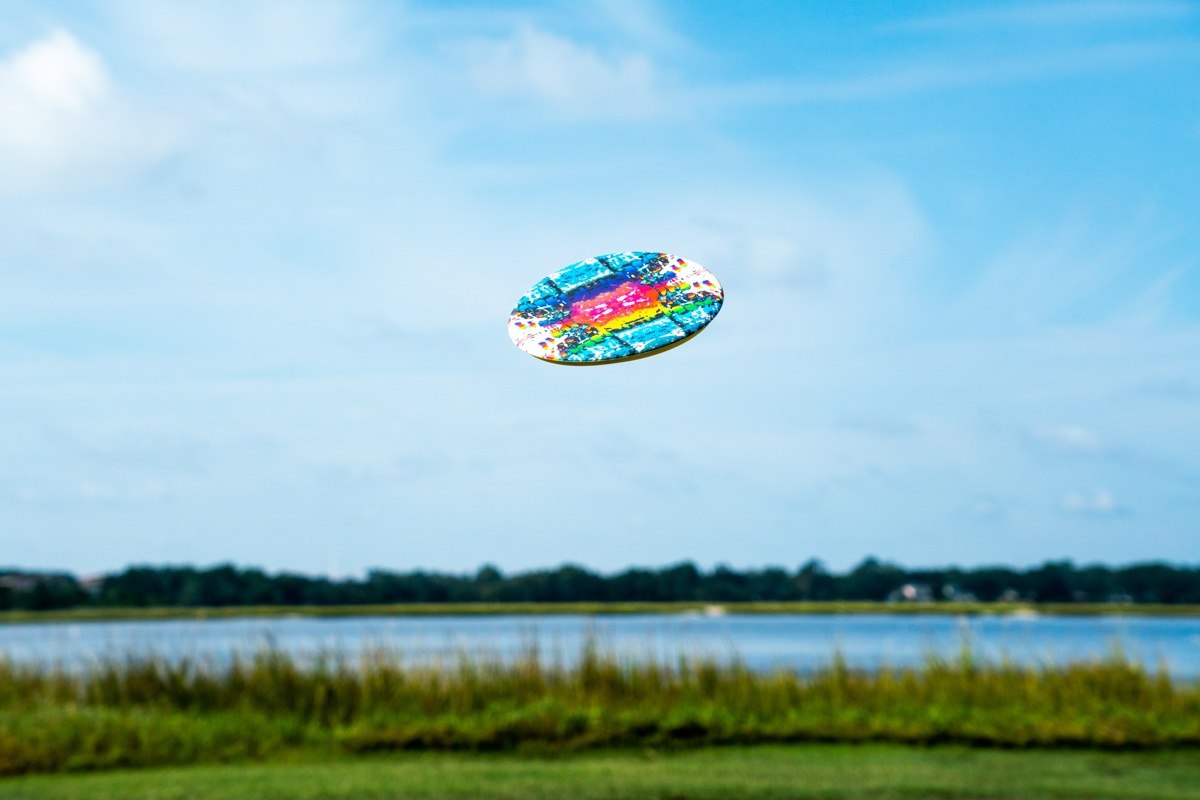Kolorowe frisbee Waboba Wingman Pro lecące nad zielonym polem i jeziorem w tle