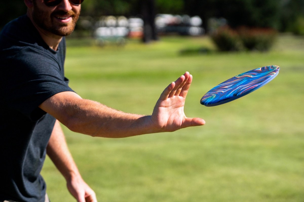 Mężczyzna rzucający kolorowe frisbee Waboba Wingman Pro na otwartym zielonym trawniku
