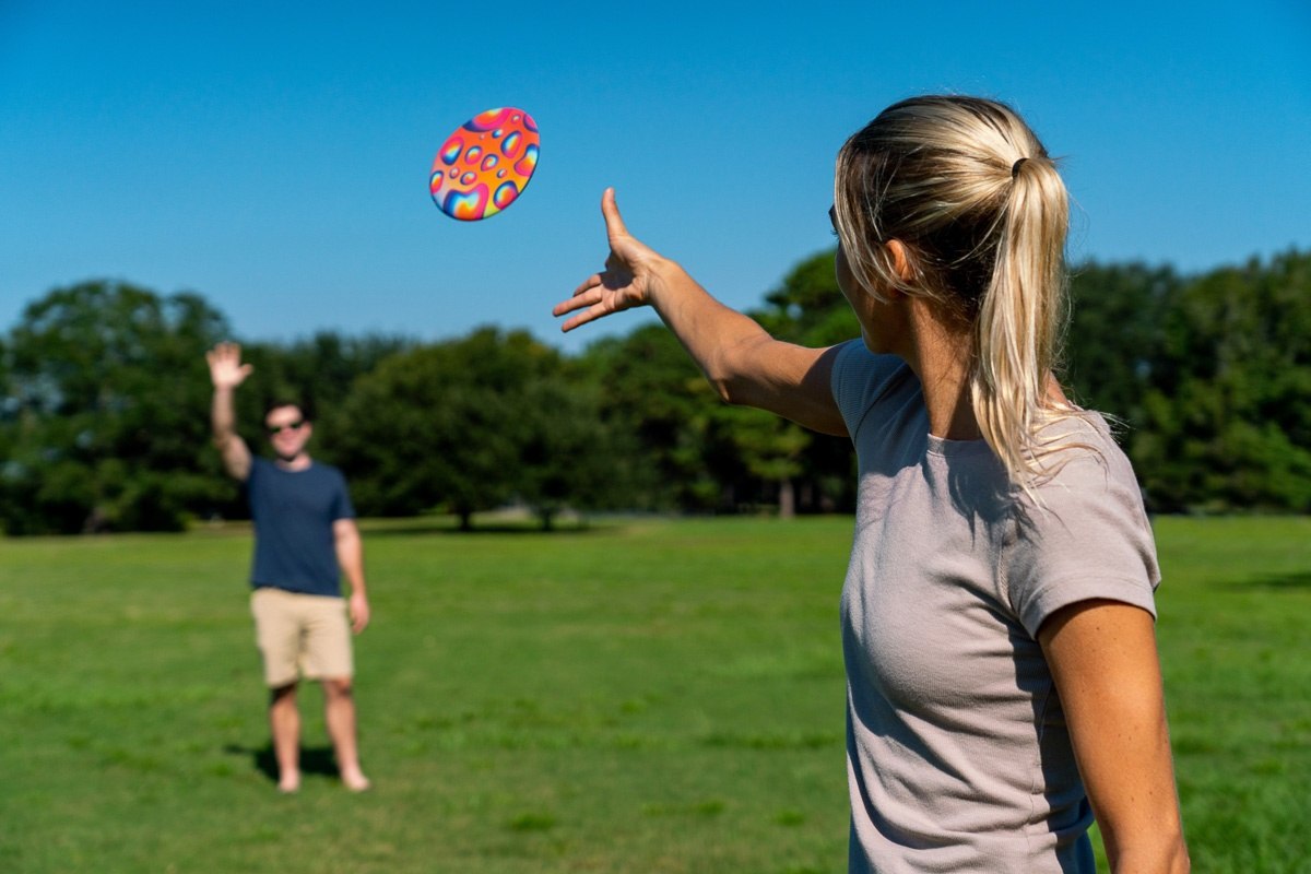 Kobieta rzuca frisbee Waboba Wingman Retro Palm podczas gry na otwartym zielonym polu