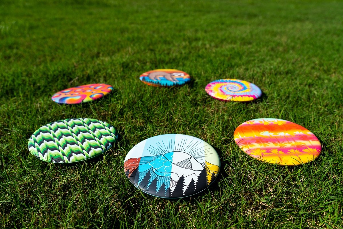 Kolorowe frisbee Waboba Wingman rozrzucone na trawie z różnymi wzorami artystycznymi