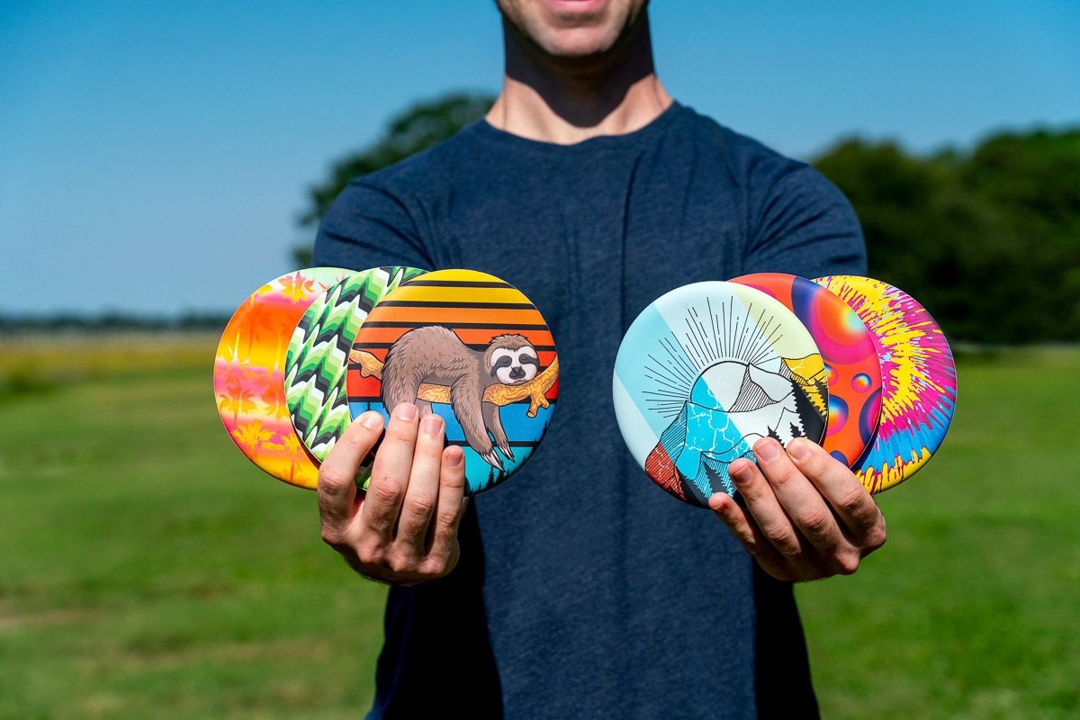 Frisbee Waboba Wingman z kolorowymi wzorami trzymane przez osobę na zewnątrz na tle zielonej trawy i niebieskiego nieba