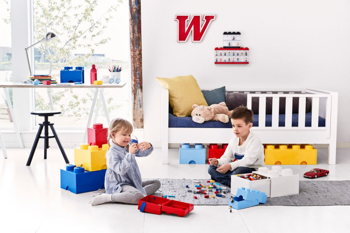 Dzieci bawiące się klockami LEGO w pokoju z nowoczesną gablotką na minifigurki LEGO na ścianie