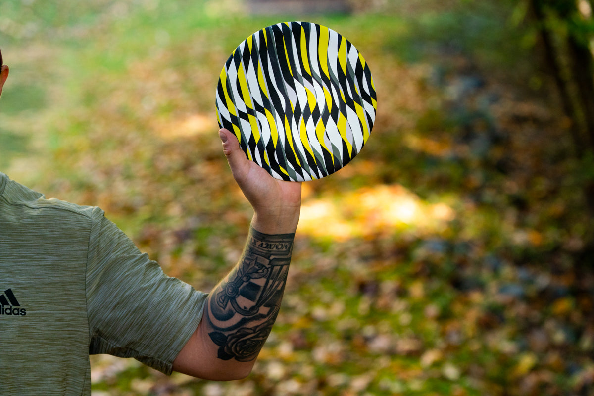 Męska ręka trzyma kolorowe frisbee Waboba Wingman Pro na tle rozmytego parku