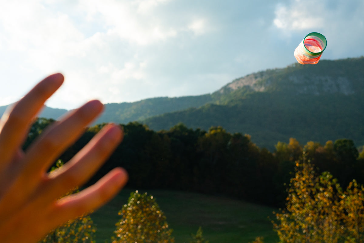 Rzutka Waboba Airlyft wyrzucana ręką na tle zielonych wzgórz i nieba z chmurami