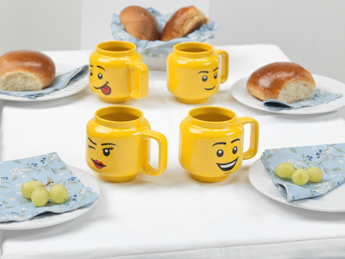Kubek LEGO ceramiczny chłopiec z żółtym kubkiem o twarzy uśmiechniętej postaci na stole z pieczywem i winogronami