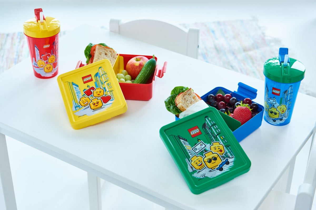 Kolorowy kubek LEGO ze słomką dla dziewczynki z zestawem pudełek na kanapki i owoce na białym stole
