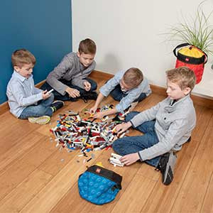 Cztery dzieci bawiące się klockami z kubełkiem LEGO na klocki firmy BV JACOB COMPANY na podłodze