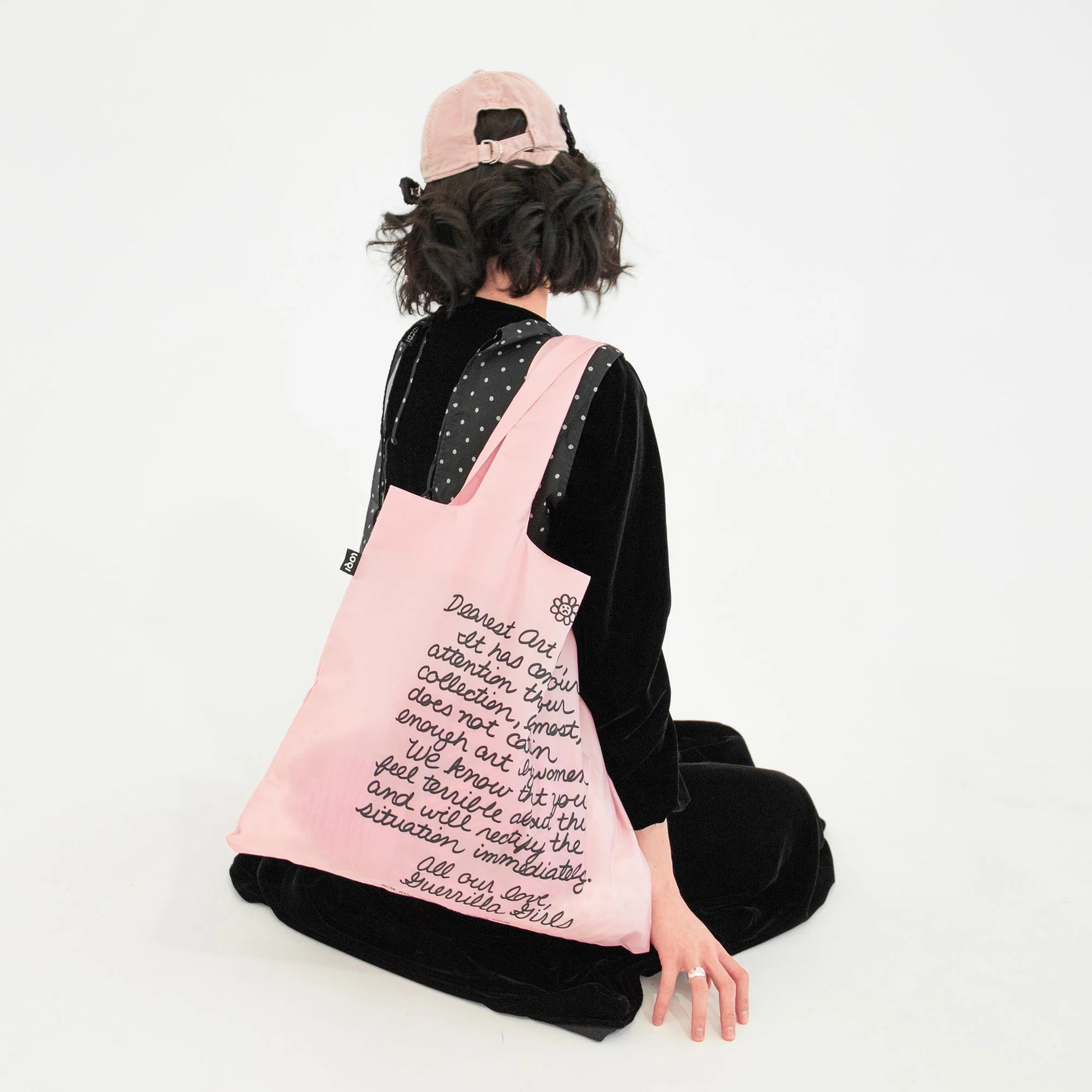 Kobieta z różową torbą LOQI Guerrilla Girls na ramieniu w casualowym stroju i różowej czapce