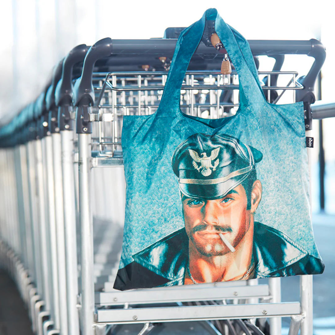 Turkusowa torba podręczna TOM OF FINLAND z nadrukiem mężczyzny w czapce na tle wózków na zakupy