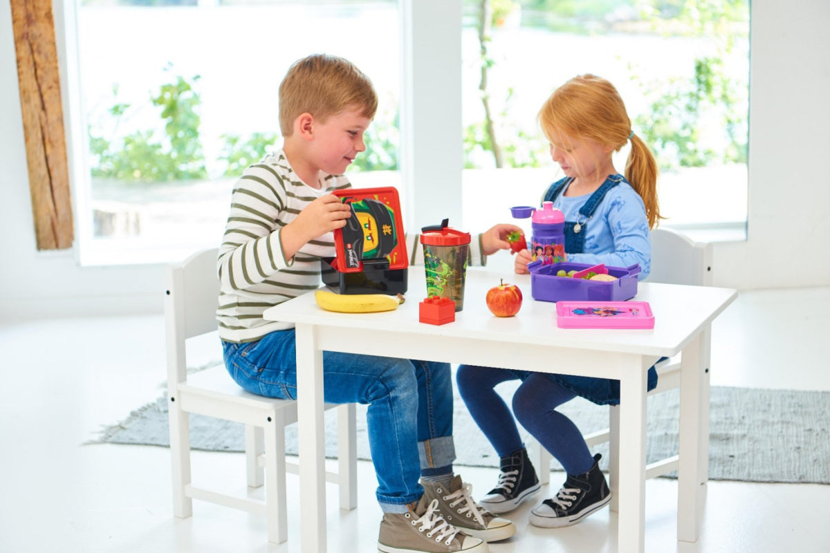 Dzieci jedzące przekąski z lunchbox LEGO Friends podczas zabawy przy białym stole