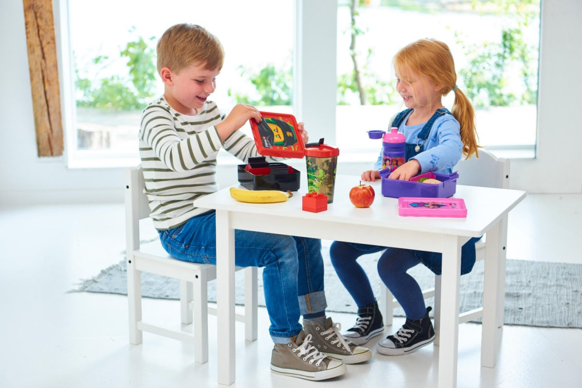 Dzieci jedzące z lunchbox LEGO Friends przy małym białym stole w jasnym pomieszczeniu