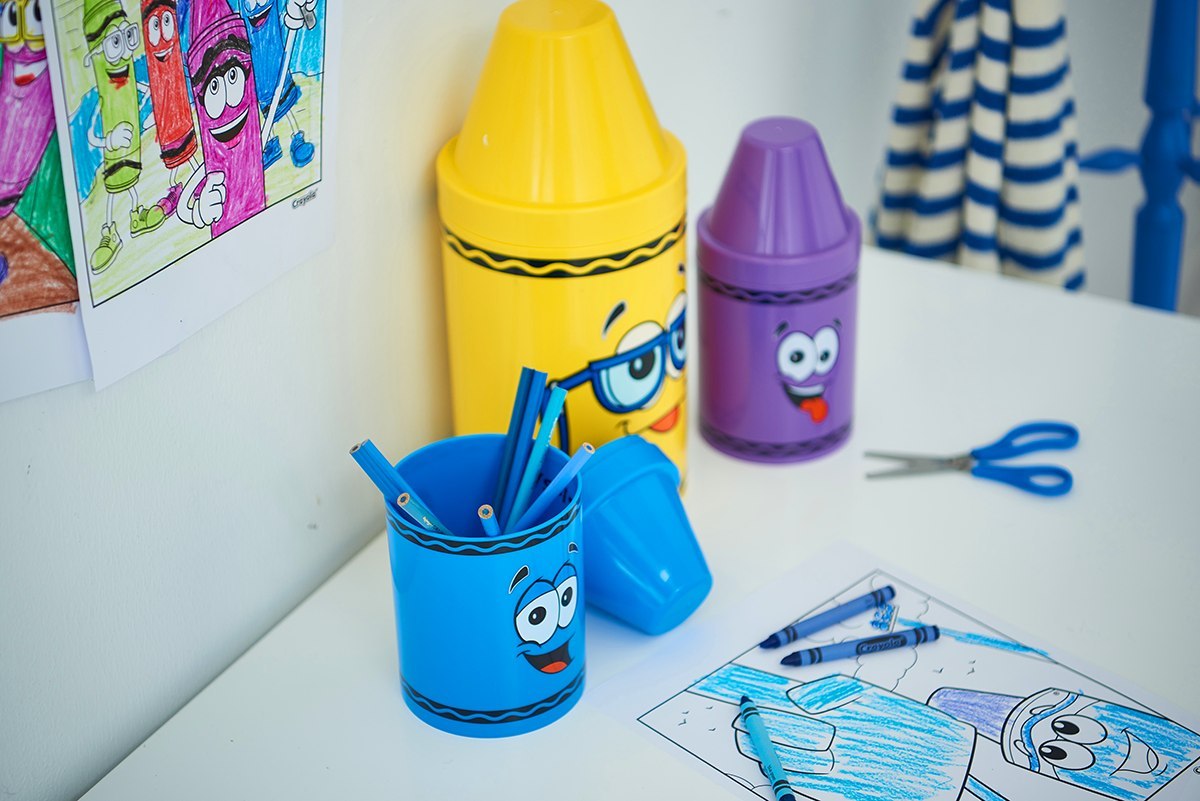 Mały pojemnik Crayola czerwony oraz inne kolorowe pojemniki na biurku z przyborami szkolnymi i kolorowanką