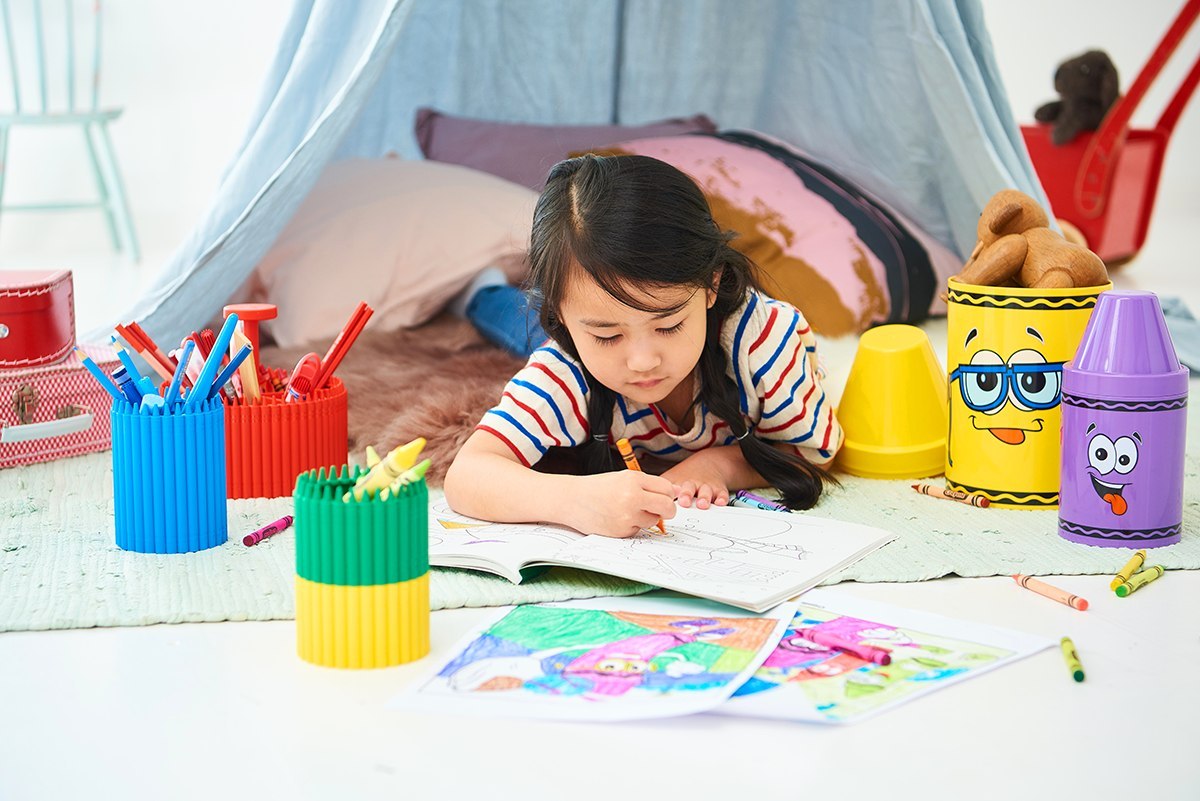 Mały pojemnik Crayola czerwony z przyborami do rysowania obok dziecka kolorującego obrazki