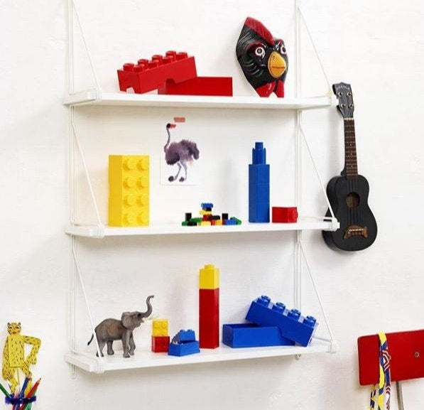 Białe półki z zabawkami w tym czerwone i żółte minipudełko LEGO 8 czerwone i niebieskie klocki oraz figurki zwierząt