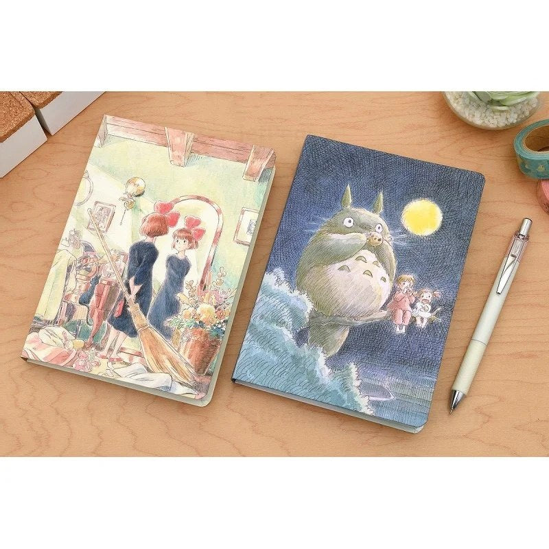 Notatnik Mój sąsiad Totoro z ilustracją postaci Totoro i dziewczyn na okładce na drewnianym stole
