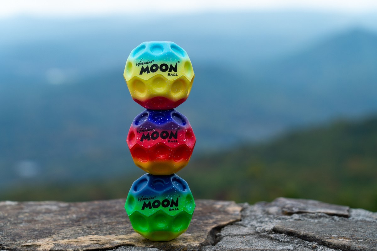 Kolorowe piłeczki Waboba Gradient Moon Ball ułożone jedna na drugiej na kamieniu z widokiem na góry