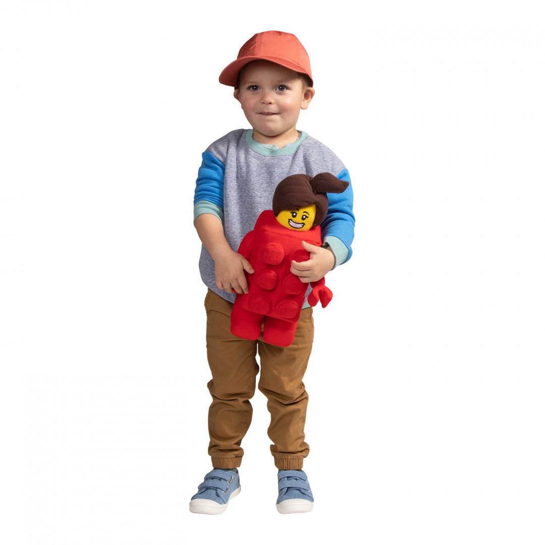 Chłopiec trzymający pluszak LEGO Brick Suit Girl w czerwonym kostiumie z uśmiechniętą twarzą