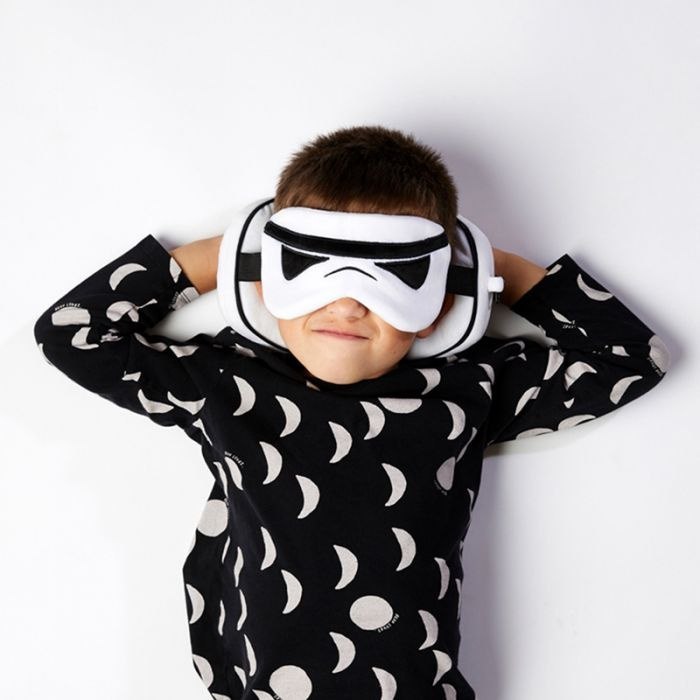 Dziecko w czarnej bluzie z białym wzorem nosi poduszkę podróżną Star Wars w kształcie hełmu szturmowca