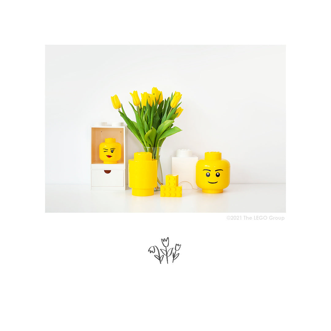 Żółty pojemnik LEGO duża głowa chłopiec obok dekoracji i żółtych tulipanów na białym tle