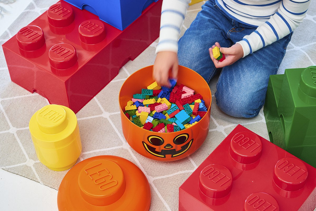Dziecko bawi się kolorowymi klockami w pomarańczowym pojemniku LEGO dynia na dywanie z klockami LEGO