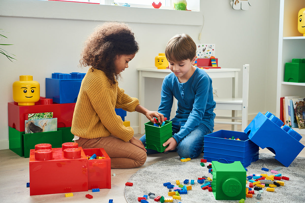 Dzieci bawiące się pojemnikiem LEGO zielony z klockami w jasnym pokoju do zabawy