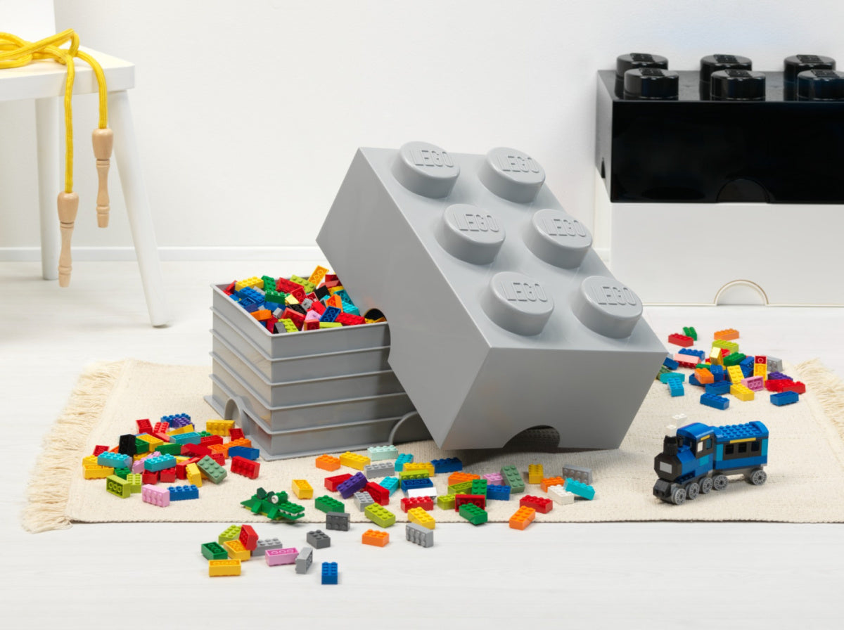 Szary pojemnik LEGO Brick 6 szary z klockami LEGO rozrzuconymi na dywanie i niebieską lokomotywą
