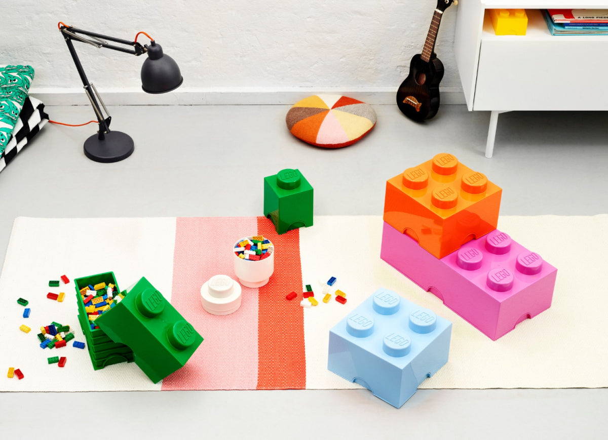 Pojemnik LEGO zielony w kształcie klocka na zabawki na białym dywanie w pokoju dziecięcym