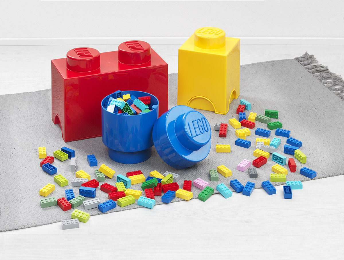 Pojemnik LEGO klocek żółty i czerwony z rozrzuconymi kolorowymi klockami LEGO na szarym dywanie