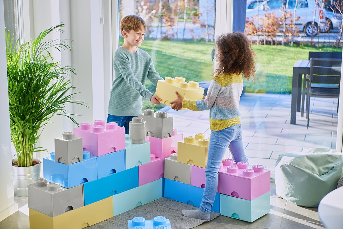 Dzieci bawiące się dużym pojemnikiem LEGO na zabawki w kształcie kolorowych klocków w jasnym pokoju