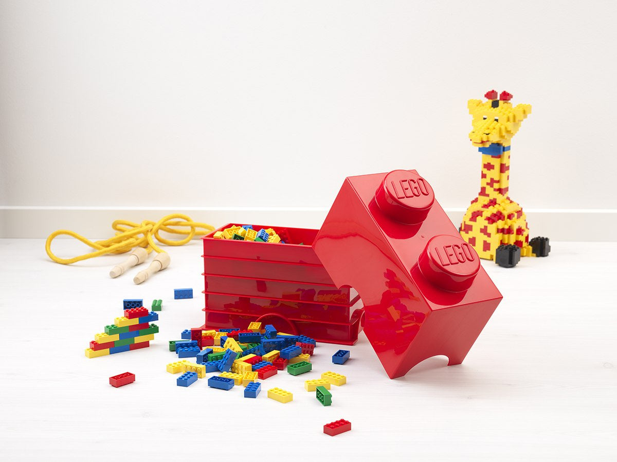 czerwony pojemnik LEGO czerwony w kształcie dużej cegiełki z rozsypanymi klocekami LEGO i figurką żyrafy