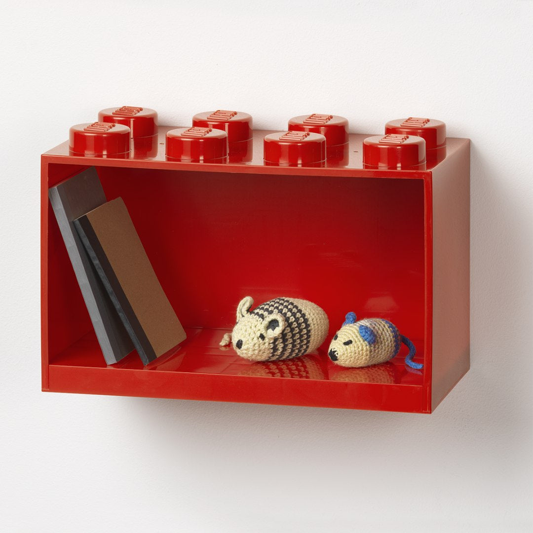 czerwona półka LEGO Brick 8 zamontowana na ścianie z książkami i zabawkami w środku