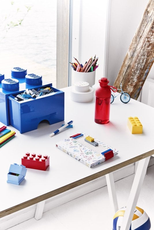 Czerwona butelka LEGO przezroczysta 500 ml na białym stole obok niebieskich i żółtych klocków LEGO