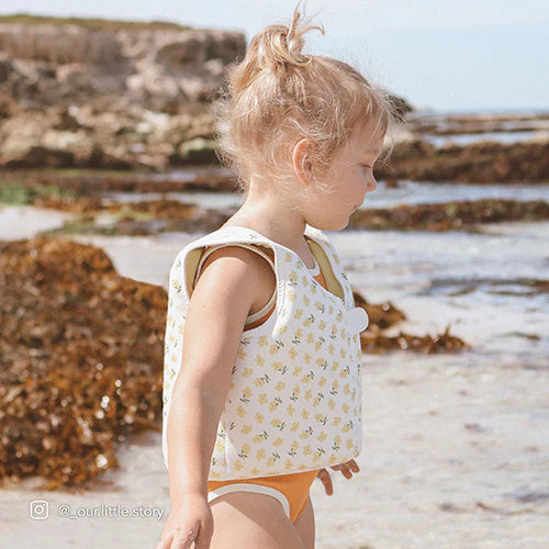 Dziecko na plaży w kamizelce do pływania dla dzieci marki SUNNY LIFE w jasnym kolorze