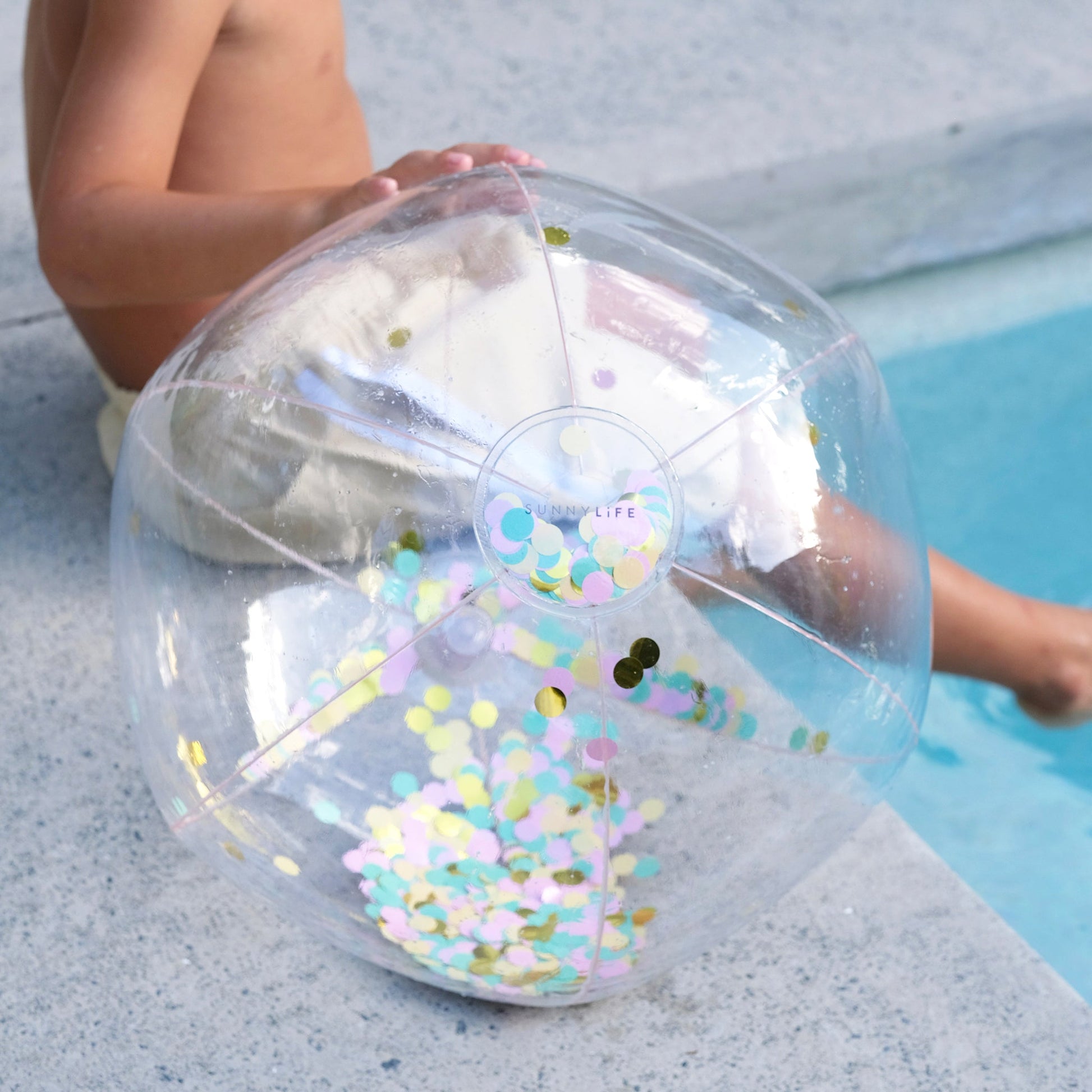 Nadmuchiwana piłka plażowa konfetti SUNNY LIFE w przezroczystym plastikowym designie nad basenem