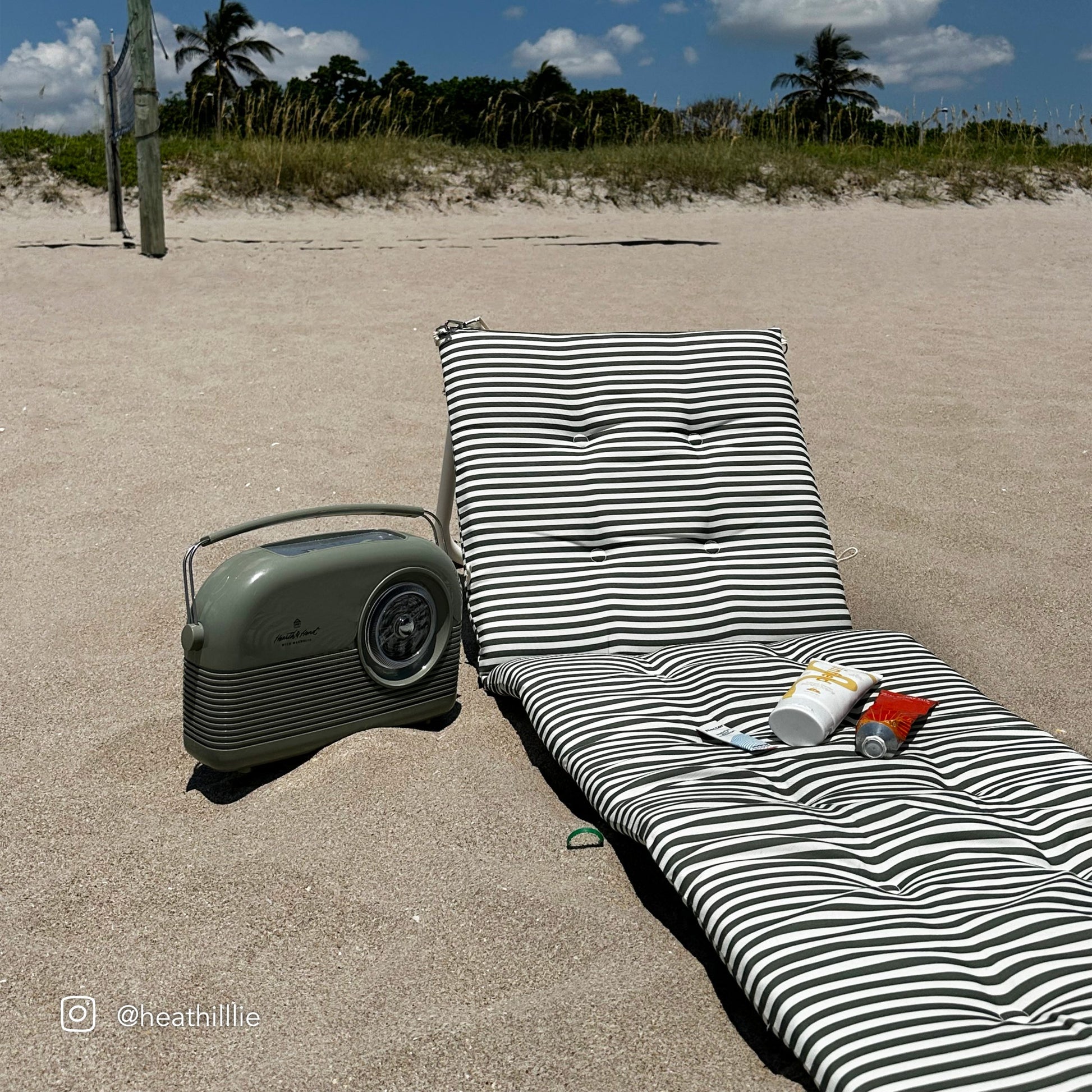 Rozkładany leżak plażowy Sunny Life w czarno-białe paski na piasku z radiem i kremami do opalania