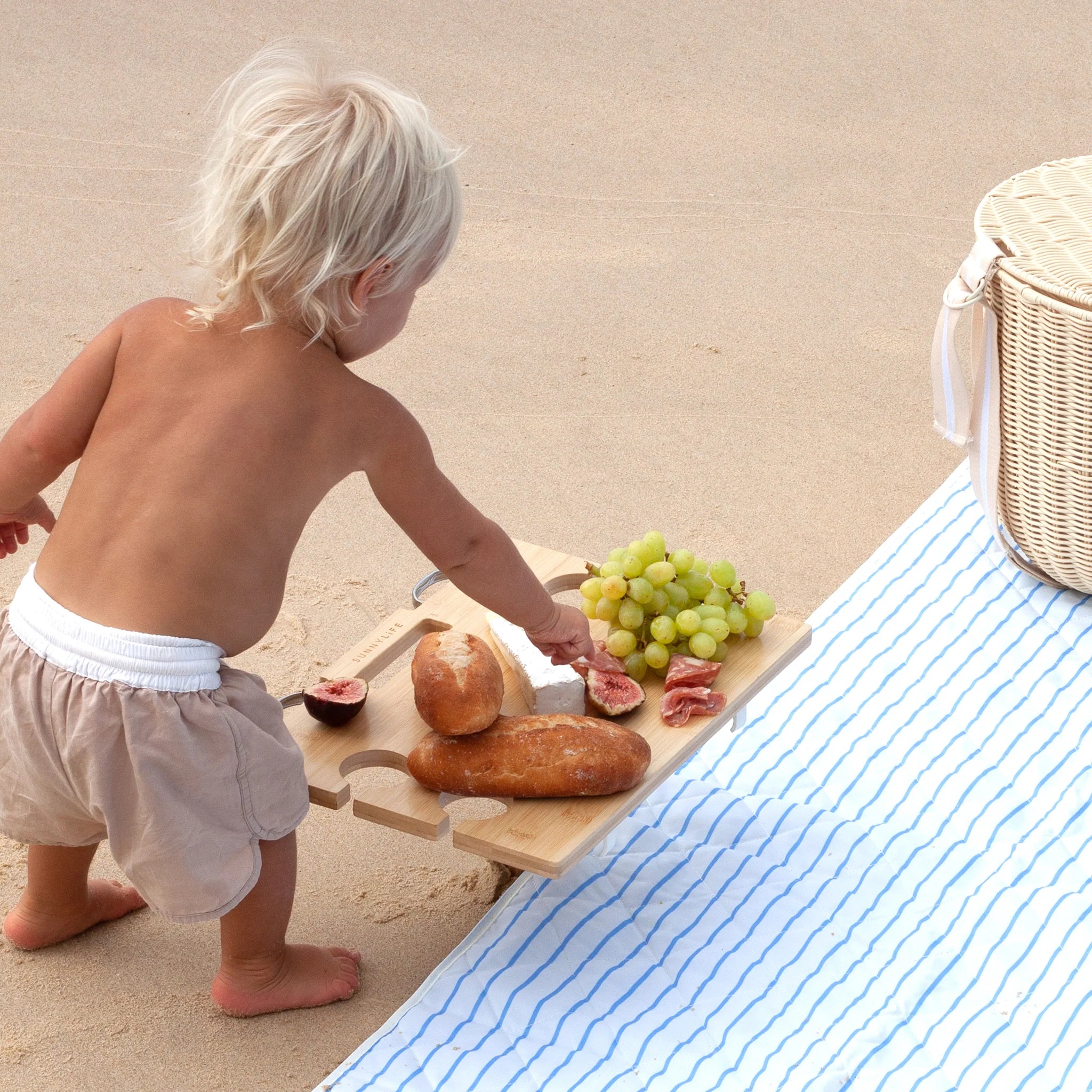 Przenośny stół piknikowy Sunny Life z jedzeniem na plaży obok dziecka i koca w paski